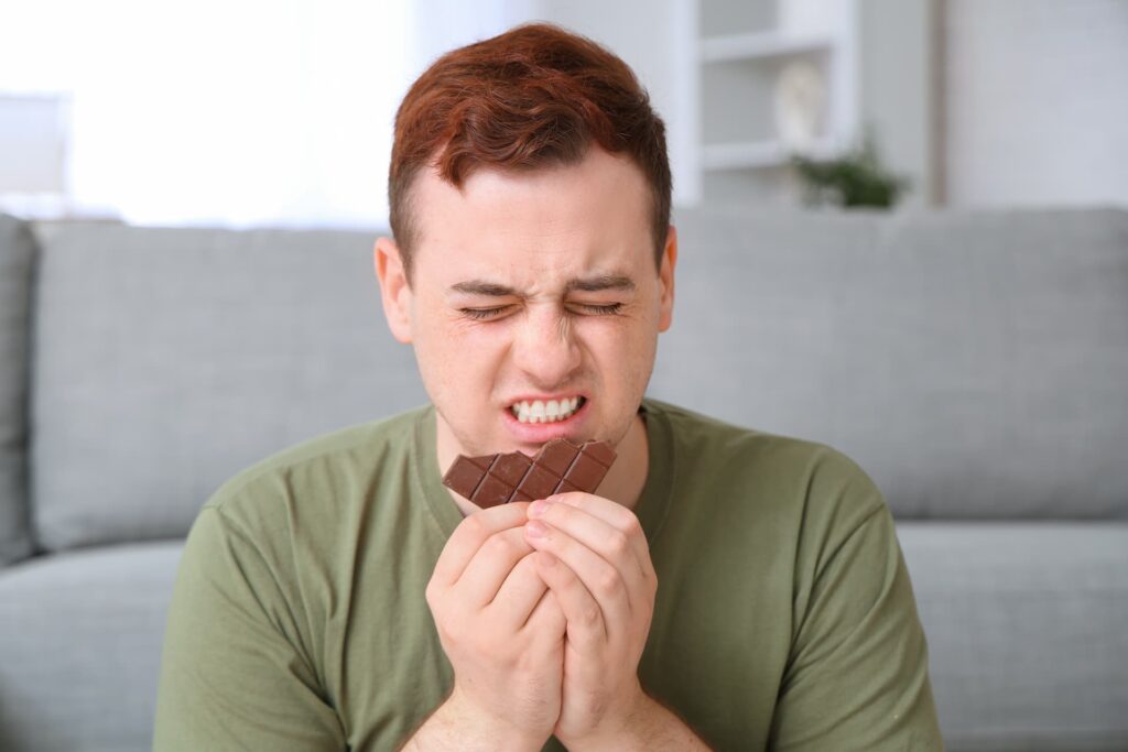 Young man eating chocolate experiencing common causes of canker sores
