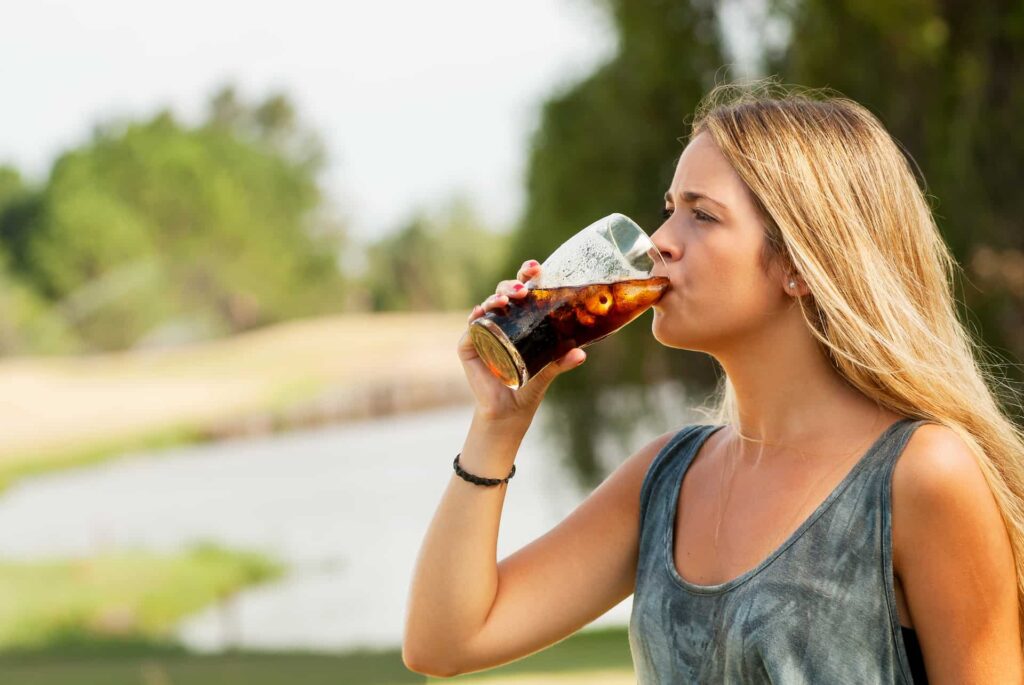 Woman with blonde hair drinking dark cola which can be a common cause of tooth erosion